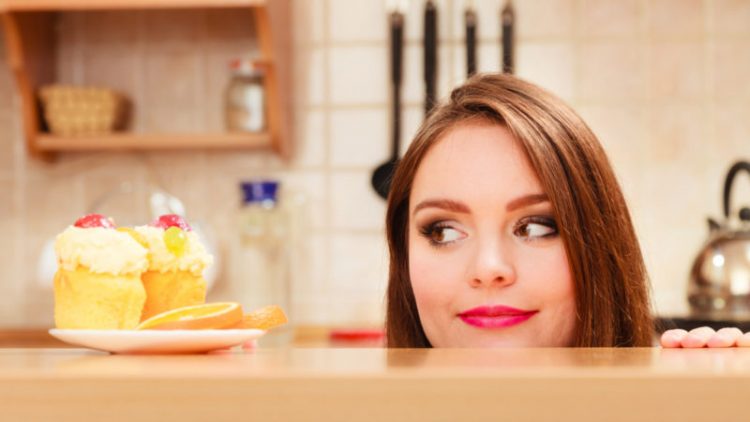 Woman hidden behind table sneaking and looking at delicious cake with sweet cream and fruits on top. Appetite and gluttony concept.